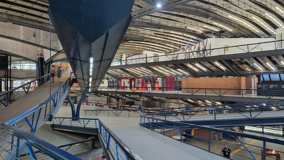 Intérieur du CCSP avec rampes bleues, passerelles, tables et toiture courbe éclairée