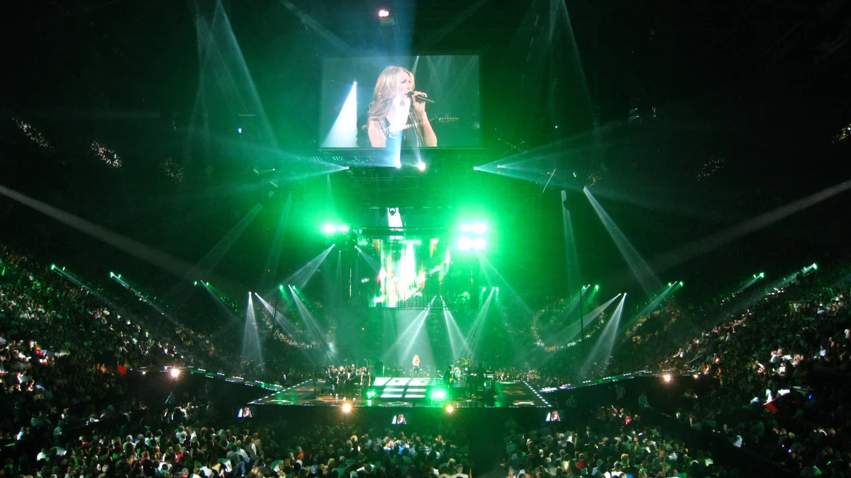 Salle comble avec une scène éclairée en vert et Céline Dion affichée sur un écran suspendu