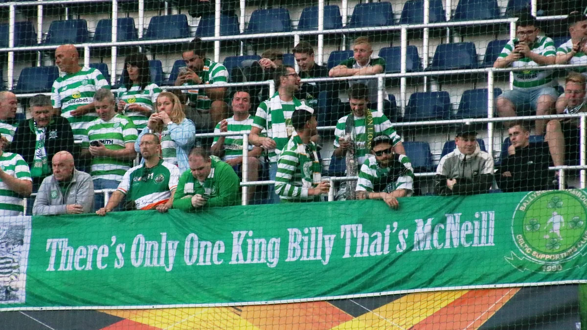 Des supporters du Celtic en maillots verts et blancs derrière une banderole verte