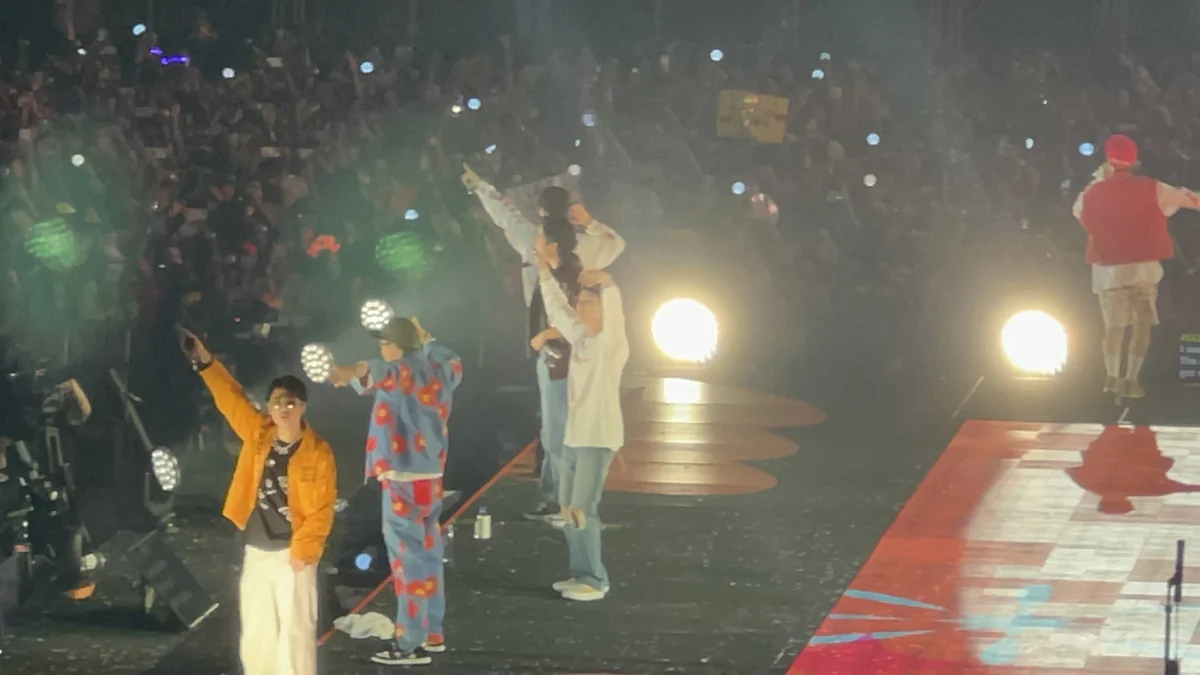 Integrantes de BTS actúan en una pasarela ante un público iluminado por light sticks.
