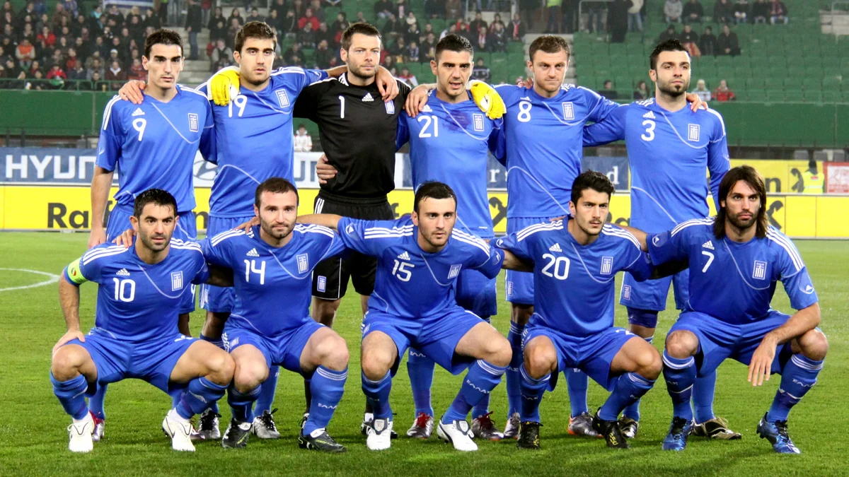 Onze jogadores da seleção grega posam em duas fileiras no gramado, com uniformes azuis e o goleiro de preto.