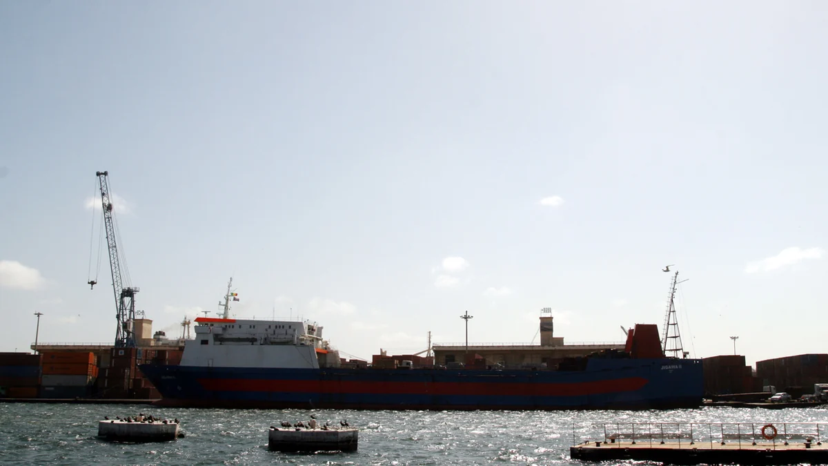 Blue-and-red ship docked beside cranes and warehouses at the Port of Dakar
