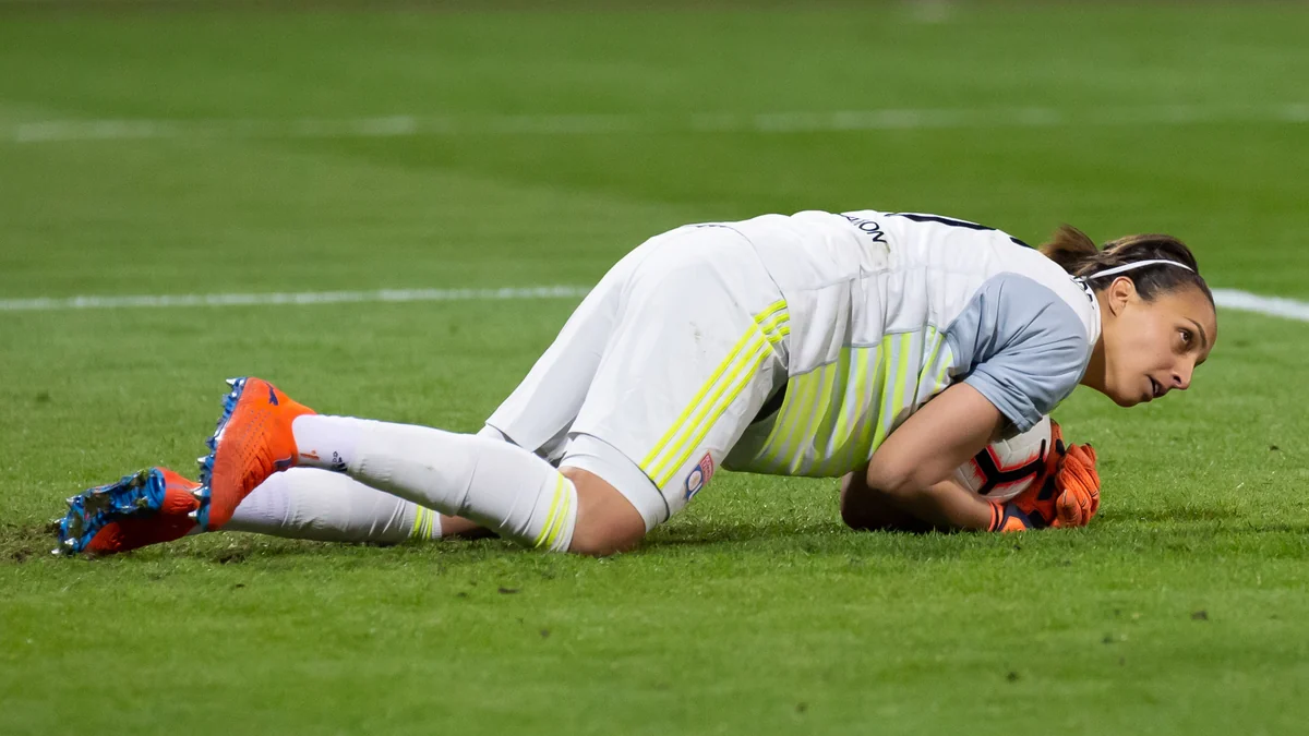 Goalkeeper in a white kit holds the ball while lying on the pitch