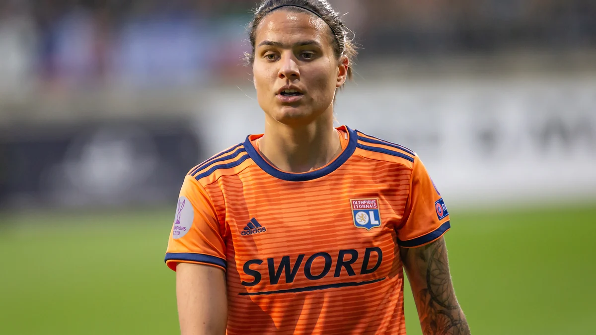 Lyon player in an orange shirt watches the match from the pitch