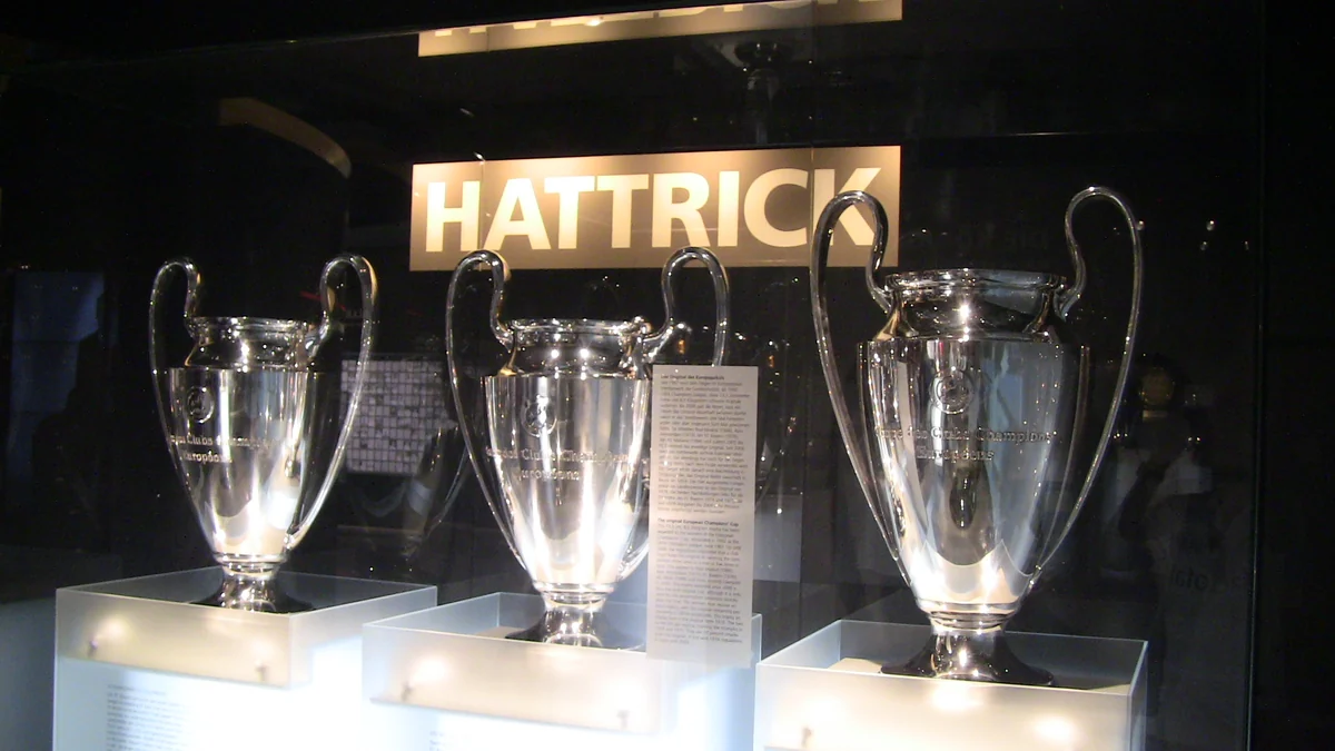 Trois coupes européennes argentées exposées dans une vitrine sous le mot Hattrick