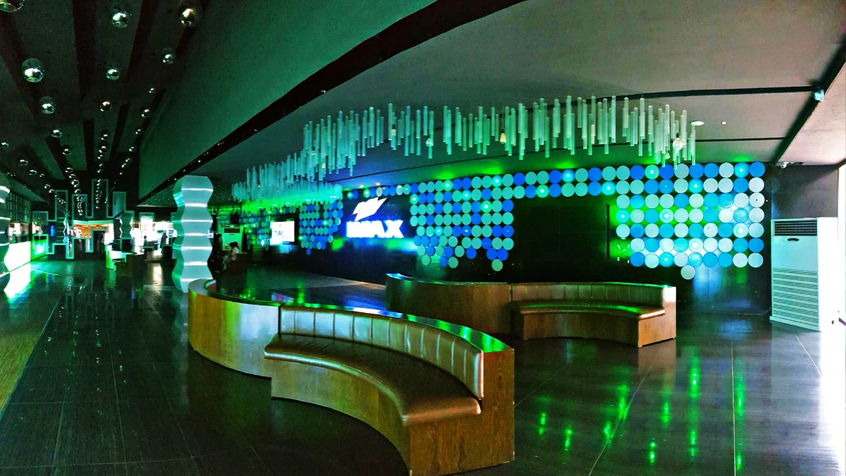 Vestíbulo de cine con bancos curvos, iluminación verde y paneles circulares
