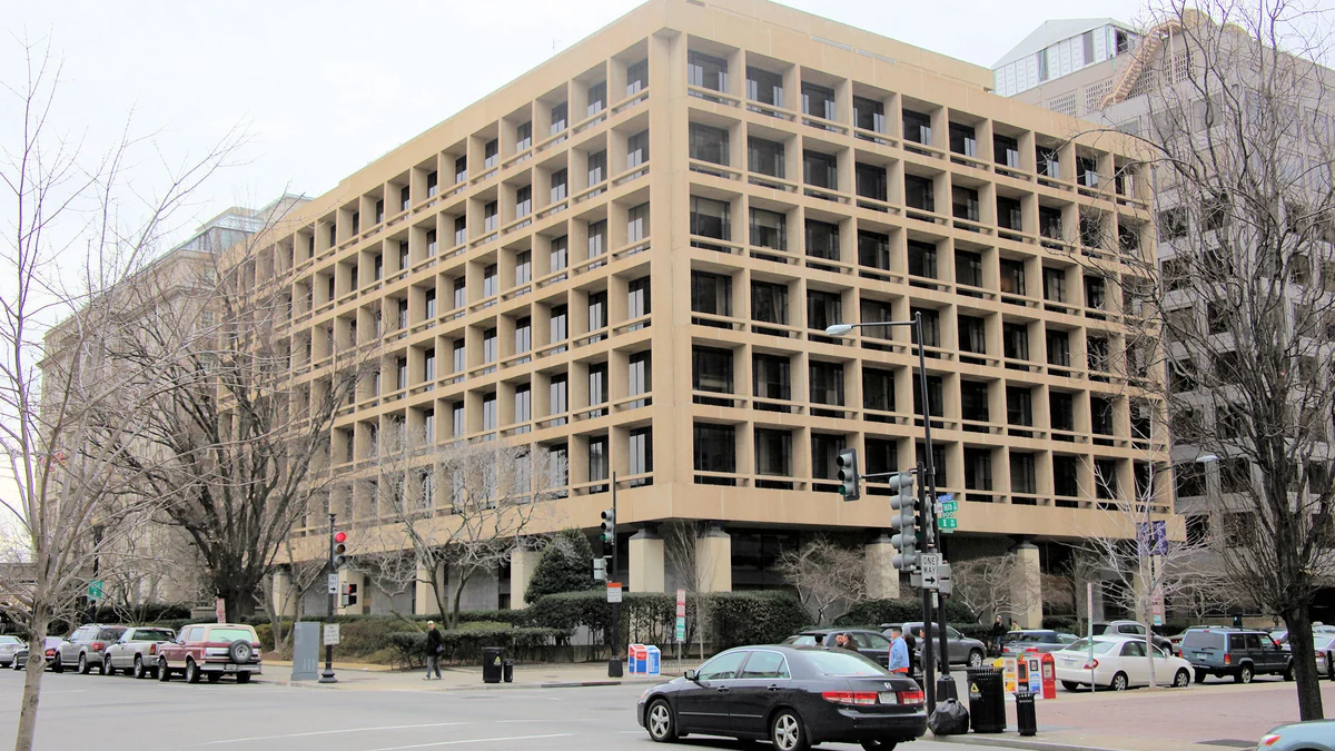 Modernist concrete building seen from a street corner, with cars and leafless trees