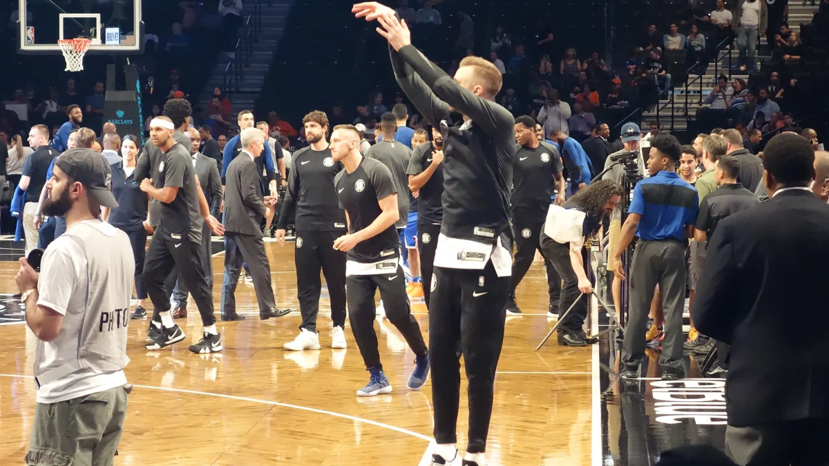 A Brooklyn Nets player takes a warm-up shot with players and staff around the court