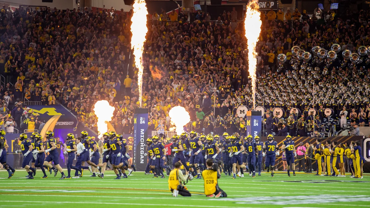 Equipe de Michigan entra no campo entre colunas de fogo diante da torcida e da banda