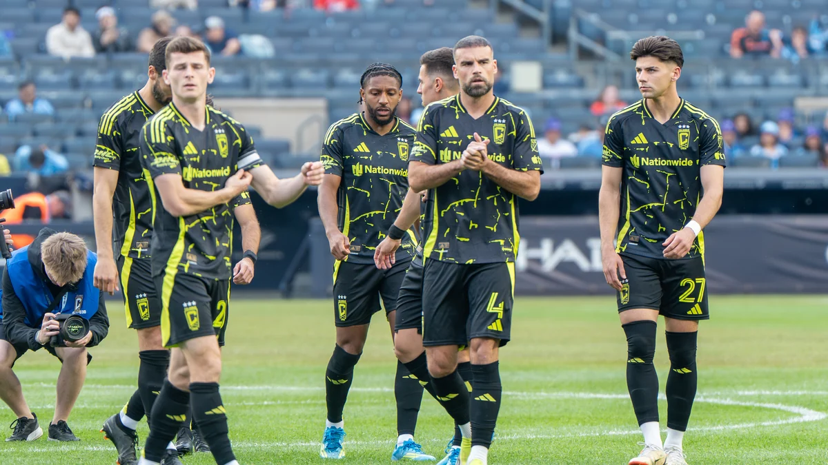 Columbus Crew players in black uniforms with yellow details walking on the field