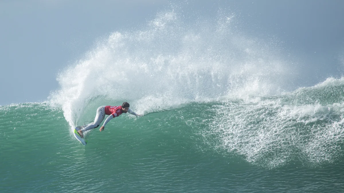 Surfista con licra roja gira sobre una ola verde y levanta una gran cortina de agua