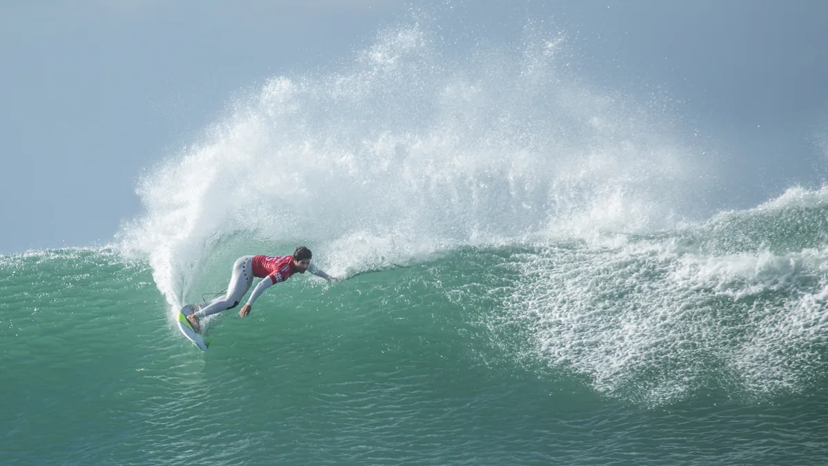 Surfista de lycra vermelha faz uma curva em uma onda verde, levantando grande spray