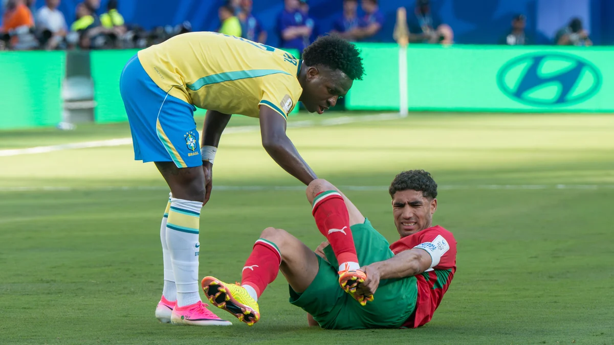 Vinícius Júnior bends toward Achraf Hakimi seated on the pitch