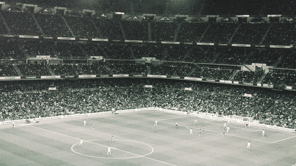 Vista ampla em preto e branco de uma partida de futebol no Santiago Bernabéu lotado de espectadores