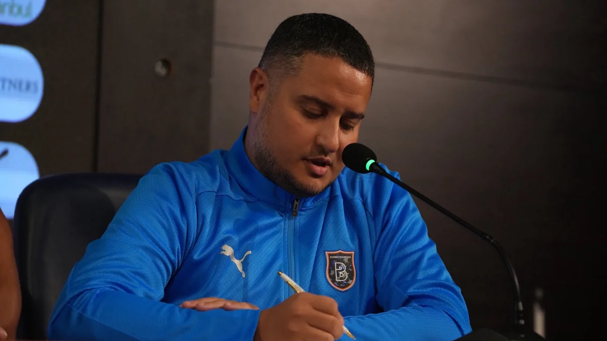 Homem com agasalho azul escreve diante de um microfone em uma entrevista coletiva