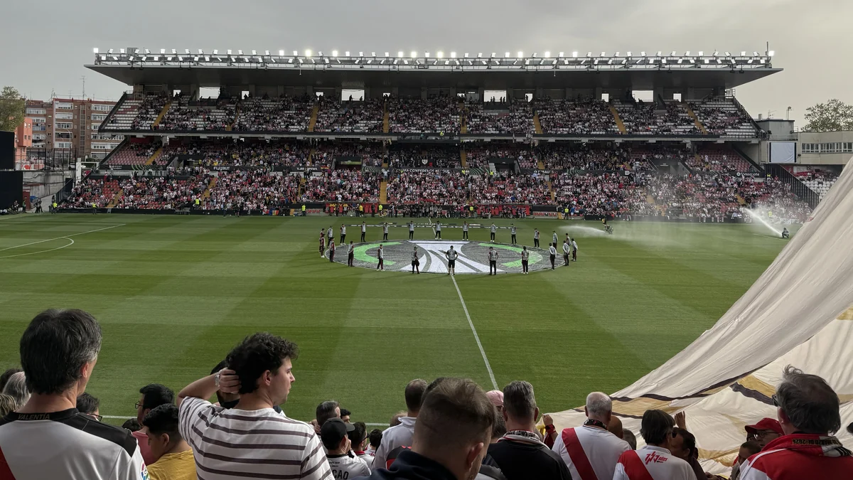 Campo de futebol visto da arquibancada, com público e uma cerimônia no círculo central