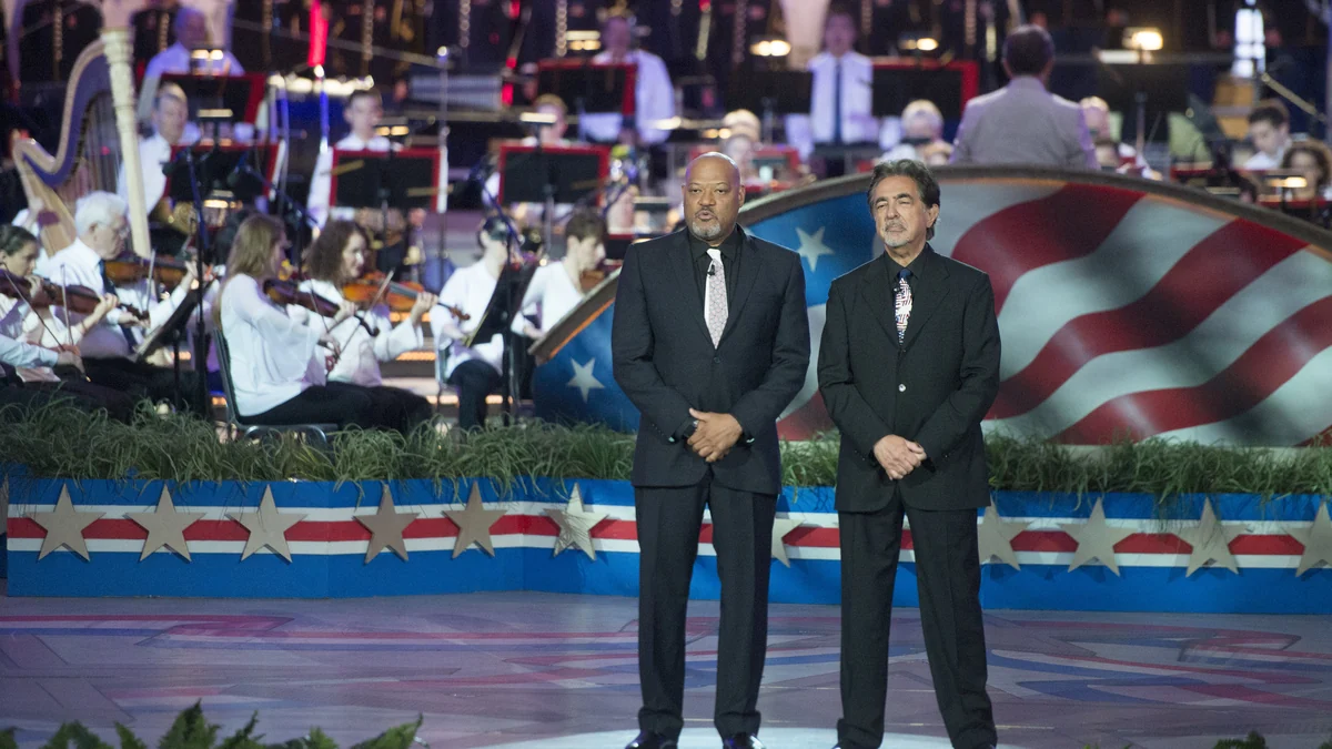 Laurence Fishburne y Joe Mantegna de traje ante una orquesta y un decorado con la bandera de Estados Unidos