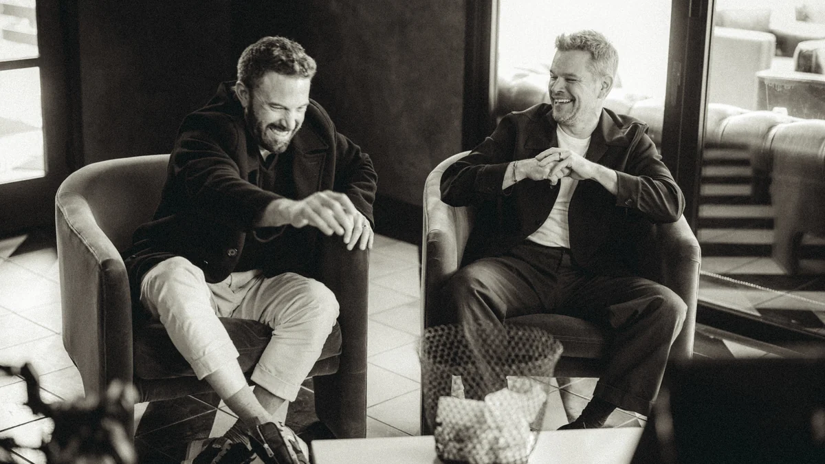 Matt Damon y Ben Affleck ríen sentados en sillones durante una entrevista en blanco y negro