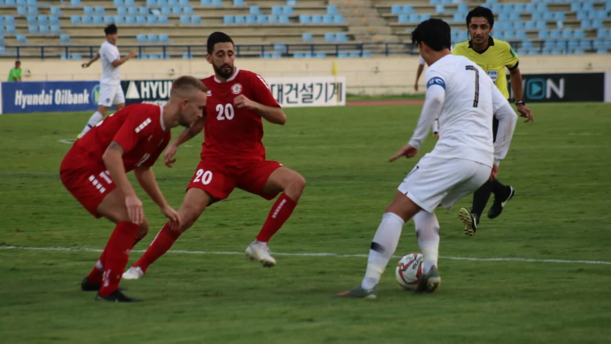 A South Korea player in white controls the ball in front of two opponents in red.