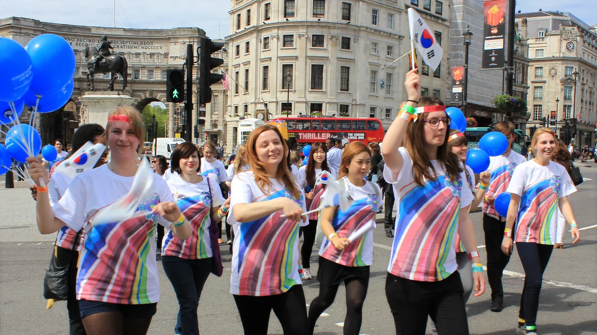 Jóvenes caminan por una avenida de Londres con globos azules y banderas surcoreanas