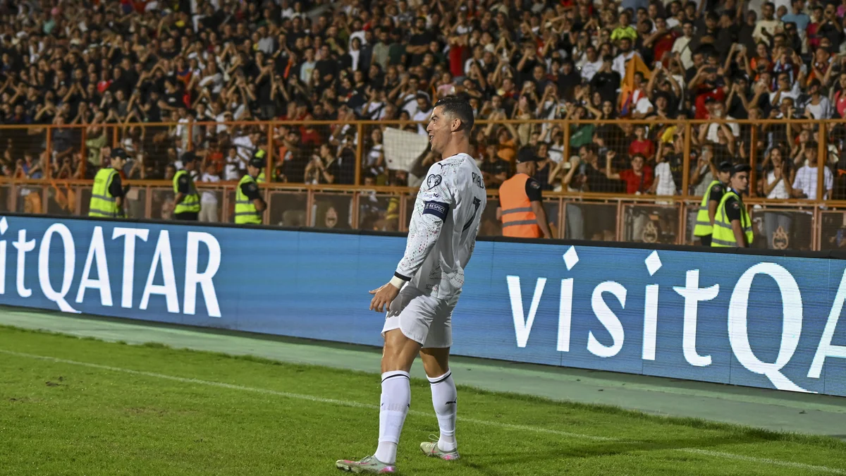 Cristiano Ronaldo comemora diante da arquibancada, próximo à lateral do campo, com o uniforme branco de Portugal