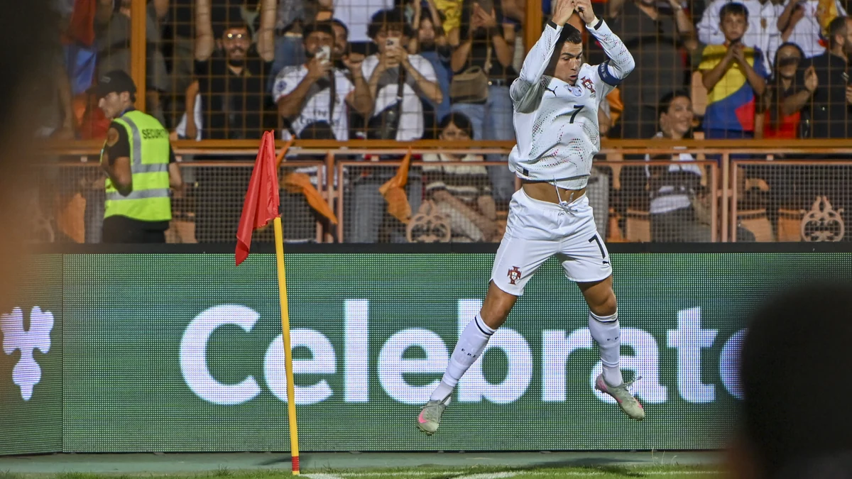 Cristiano Ronaldo salta com as mãos unidas junto à bandeira de escanteio, vestindo o uniforme branco de Portugal