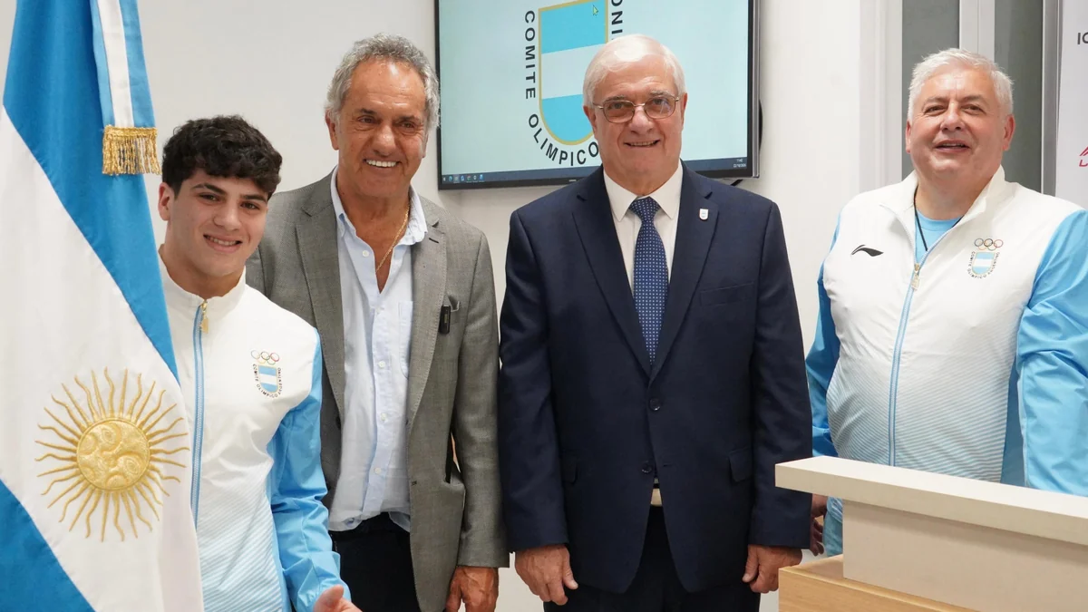Quatre hommes posent près d’un drapeau argentin, dont un jeune en tenue d’équipe olympique