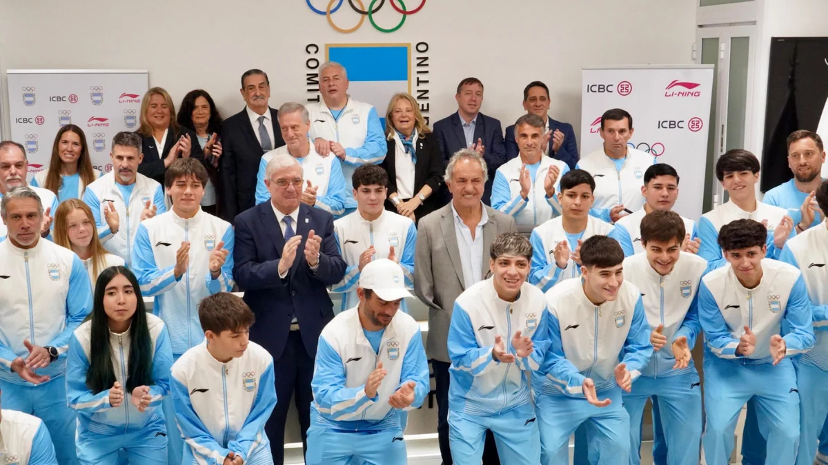 De jeunes athlètes en tenues bleues et blanches posent en groupe sous les anneaux olympiques