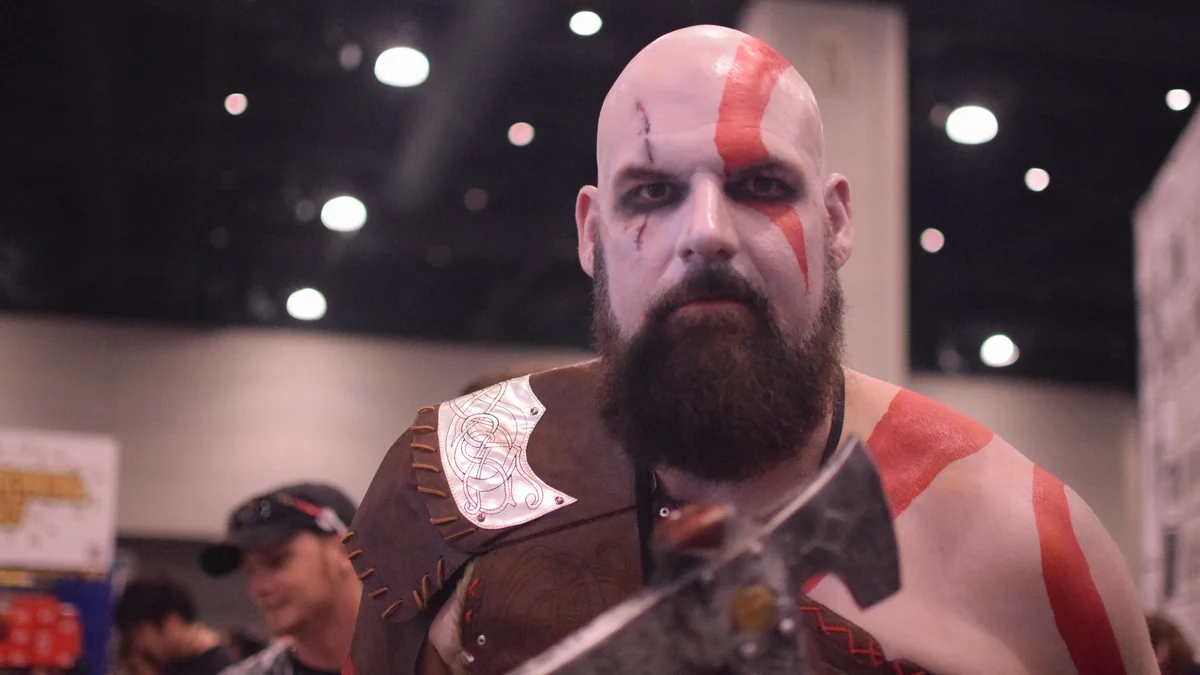 Cosplayer de Kratos em convenção, com pintura corporal e adereços inspirados no personagem.