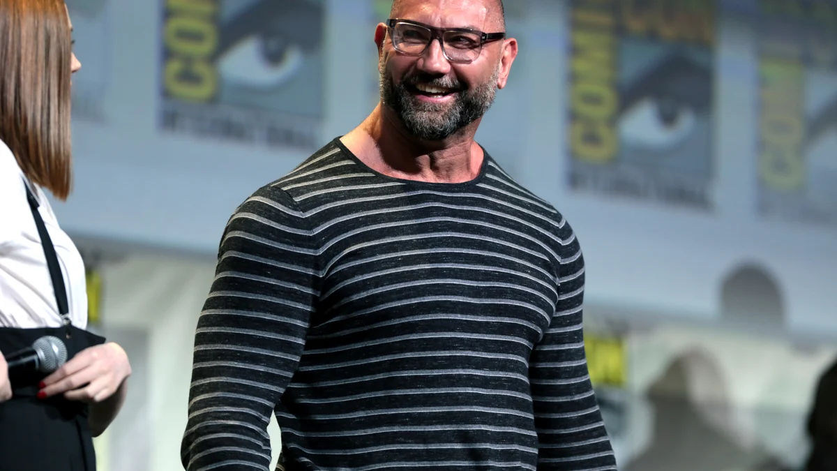 Dave Bautista em evento de tapete vermelho, olhando para os fotógrafos.