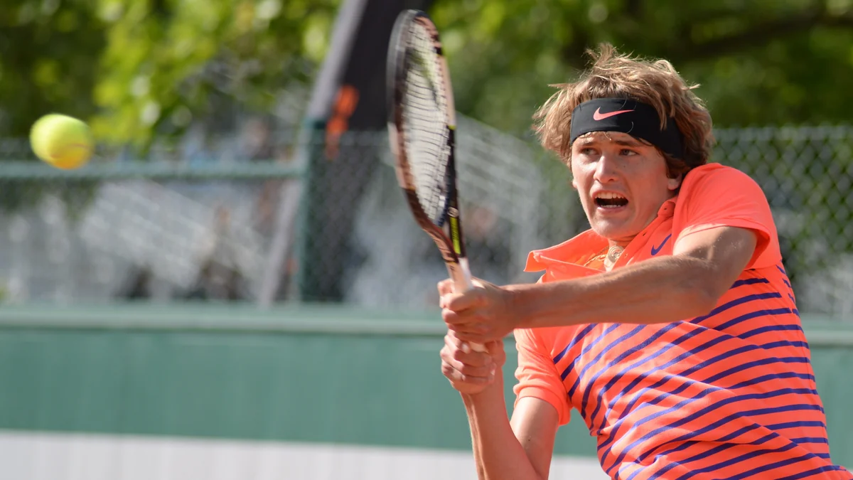 Alexander Zverev rebate uma bola com as duas mãos usando camisa laranja