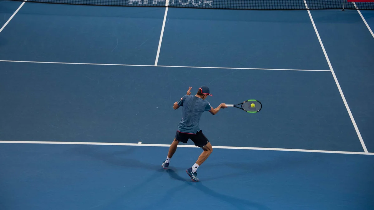Alex de Minaur golpeia a bola com o forehand em uma quadra azul