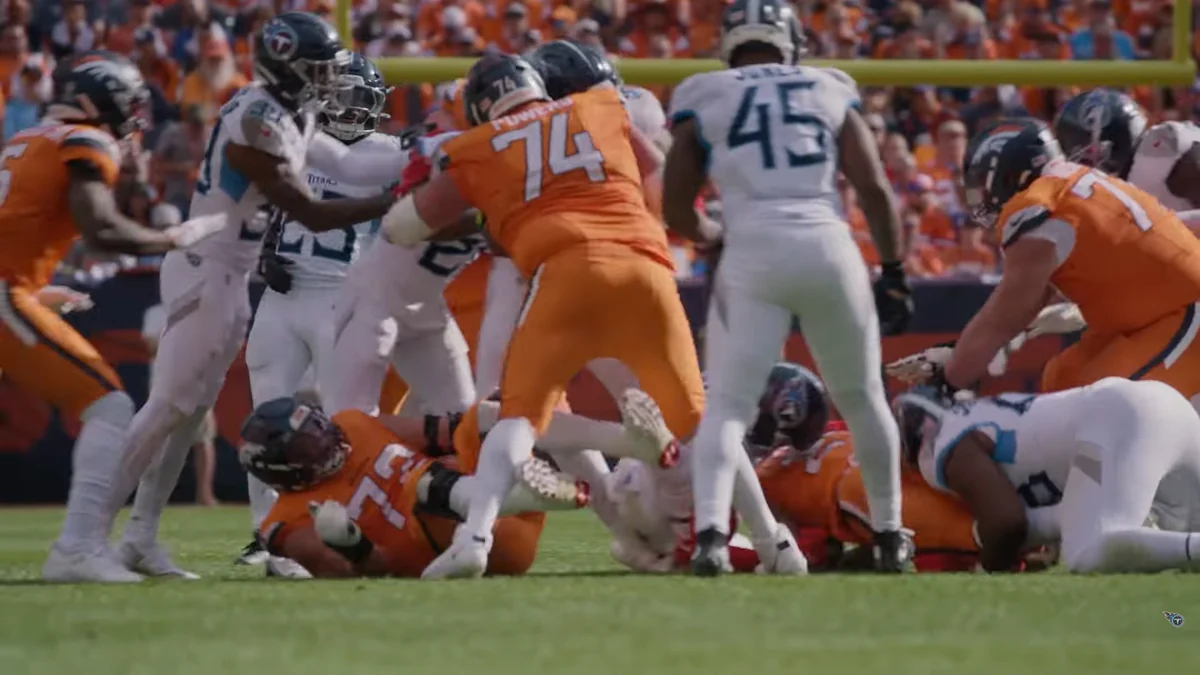 Jogadores dos Broncos e dos Titans disputam uma jogada junto ao gramado