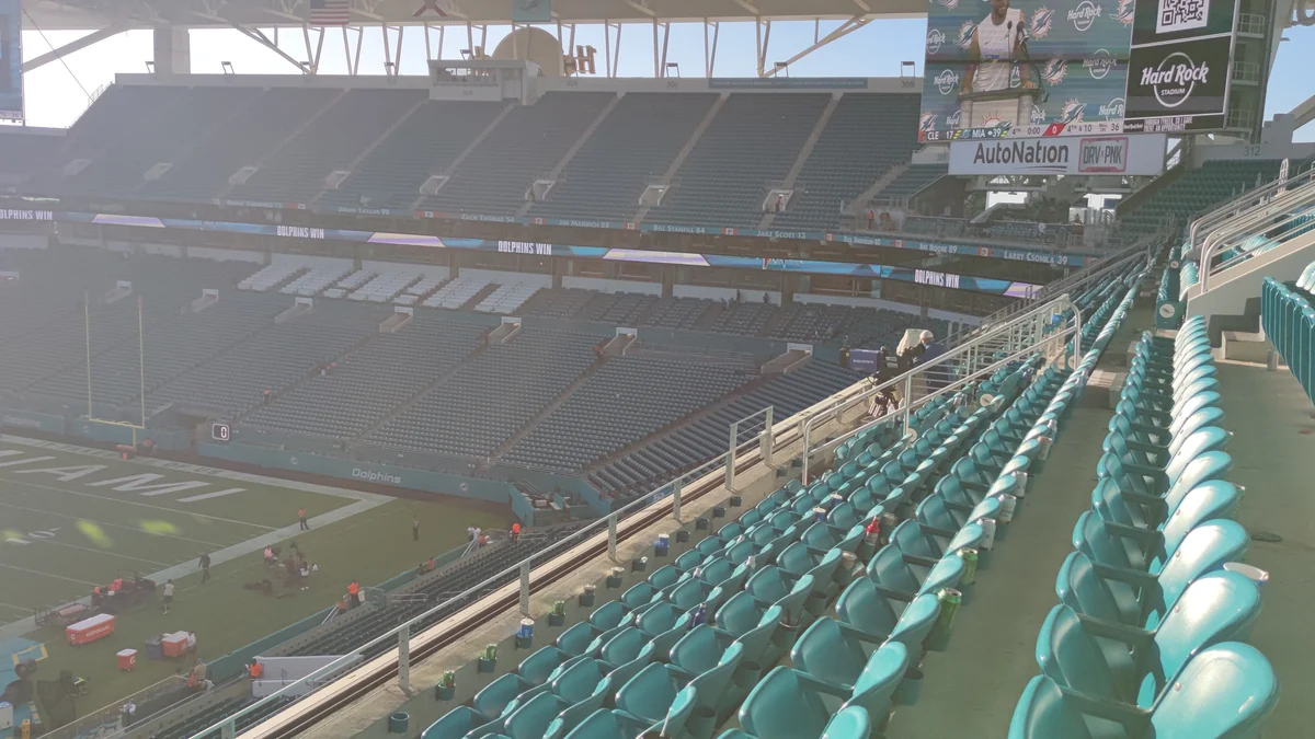 Gradas con asientos verdes frente al campo de fútbol americano de un estadio casi vacío.