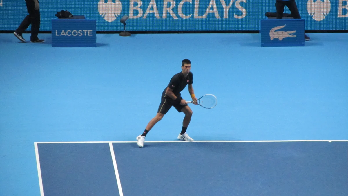 Novak Djokovic tient sa raquette en position d’attente sur un court bleu en salle