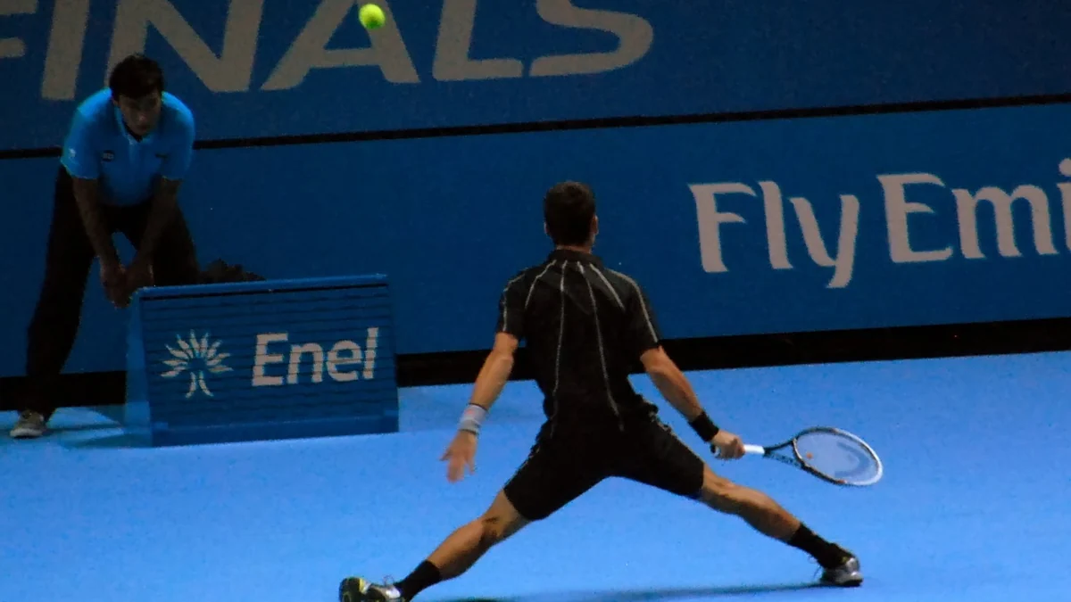 Novak Djokovic vu de dos pendant un échange sur un court bleu en salle