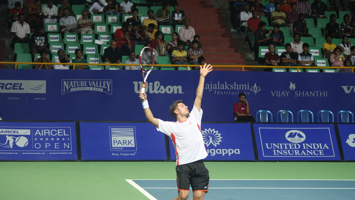 Stan Wawrinka tosses the ball to serve on a tennis court in front of the stands.