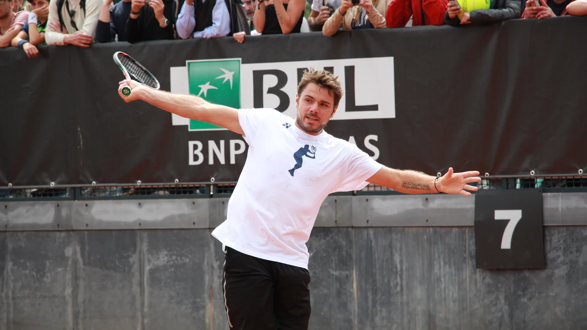 Stan Wawrinka hits the ball during practice on a clay court, with spectators behind him.