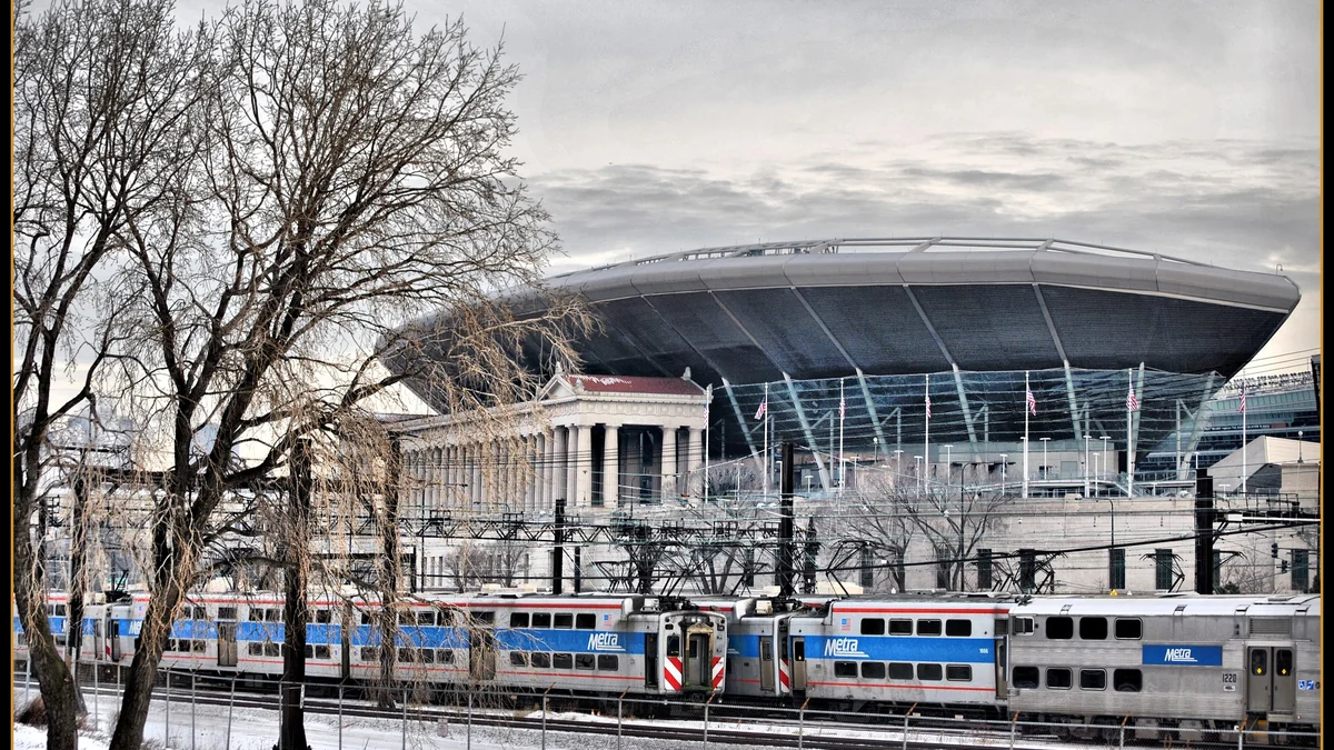 Stadium exterior behind Metra trains and leafless trees