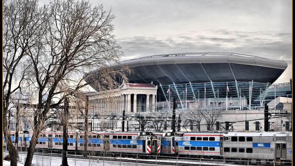Exterior de um estádio atrás de trens da Metra e árvores sem folhas