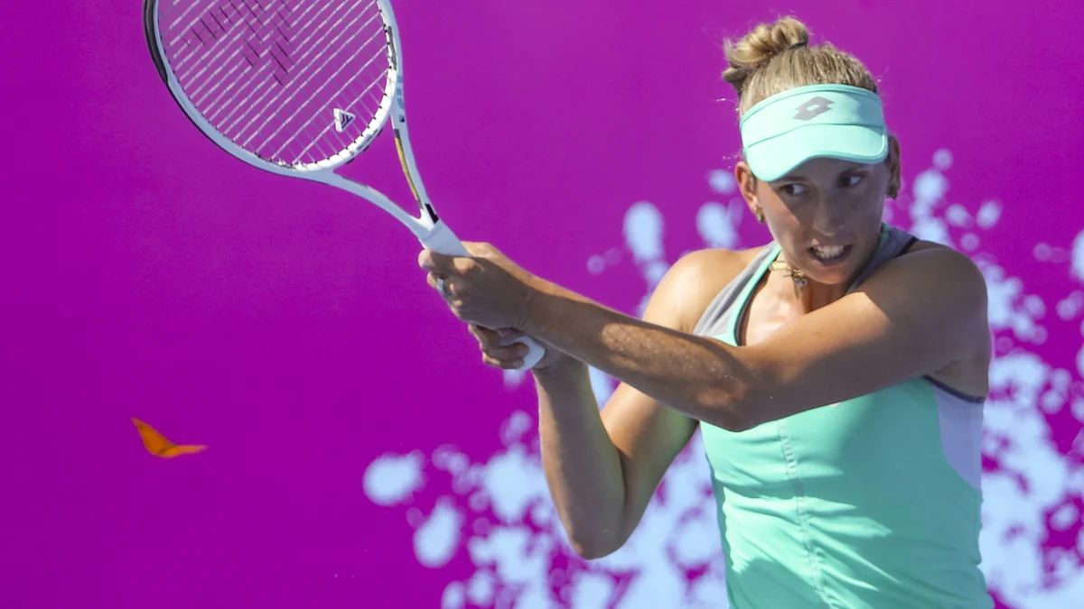 Elise Mertens prepara una devolución con la raqueta levantada ante un fondo magenta