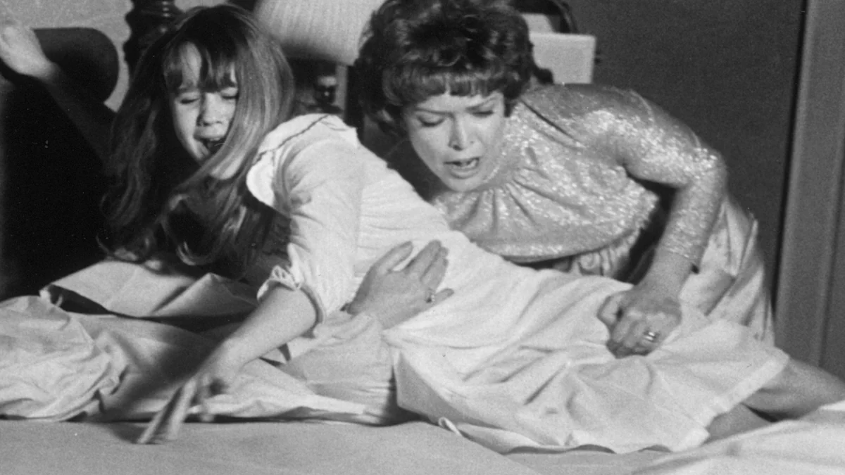 Ellen Burstyn se penche sur un lit en tenant une jeune fille dans une scène en noir et blanc.
