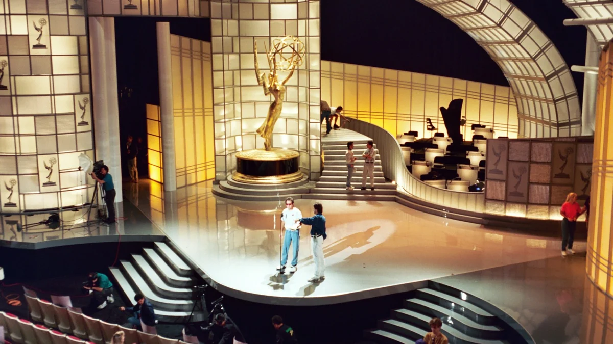 Equipe trabalha em um palco iluminado com uma grande estatueta dourada do Emmy ao centro