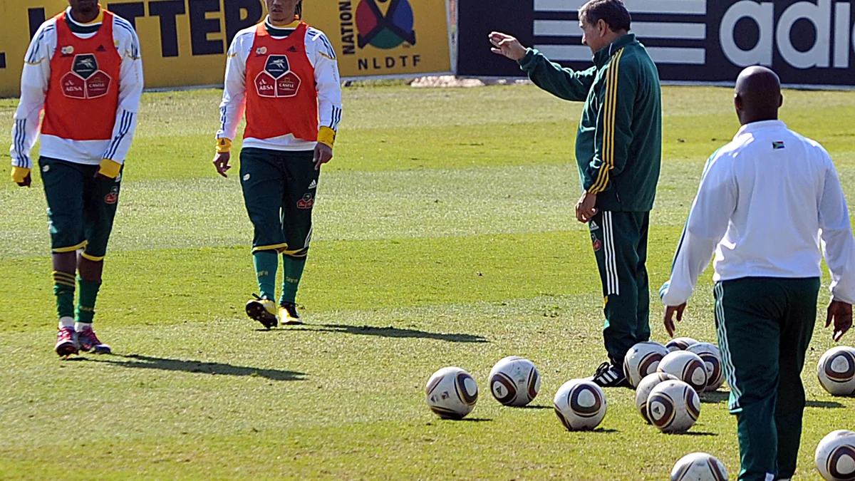 Coach instructs South Africa players beside several footballs on the pitch