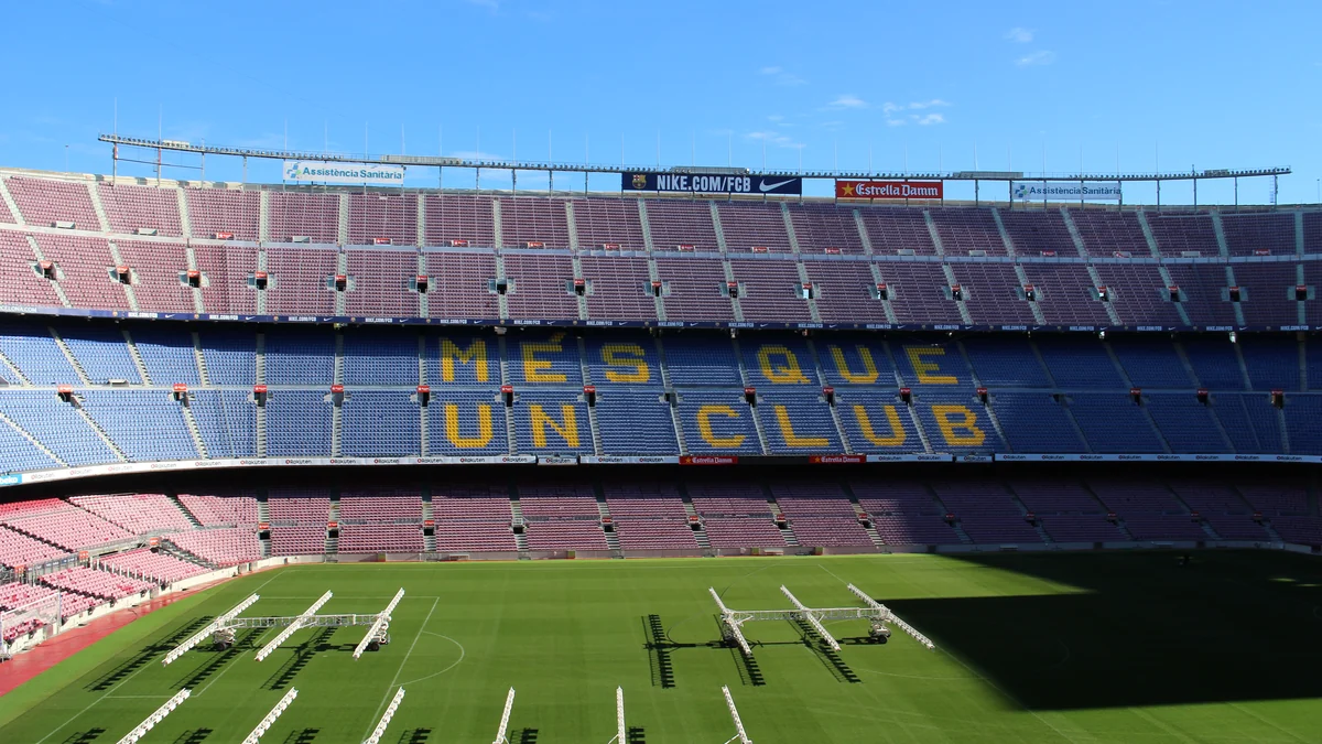 Tribunes du Camp Nou sous un ciel bleu, avec Més que un club sur les sièges et des structures métalliques sur la pelouse
