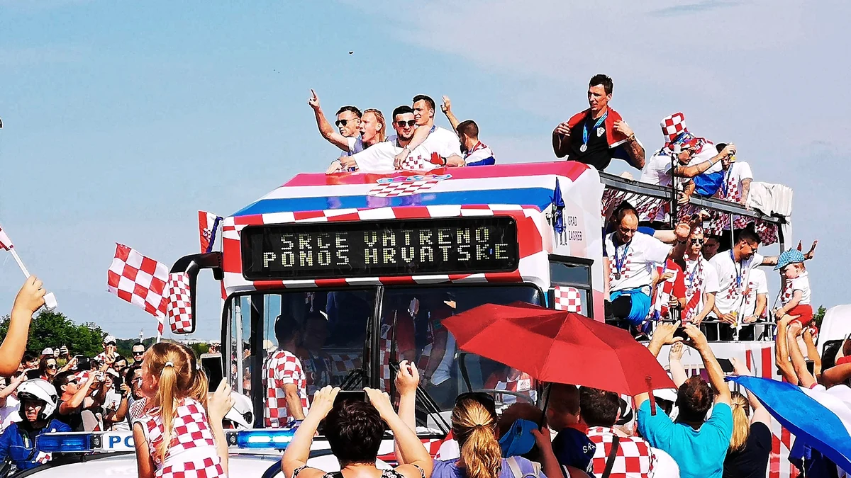 Croatia players on an open-top bus surrounded by supporters carrying checkered flags