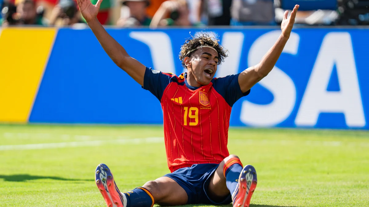 Lamine Yamal sits on the pitch with both arms raised while wearing Spain’s number 19 shirt