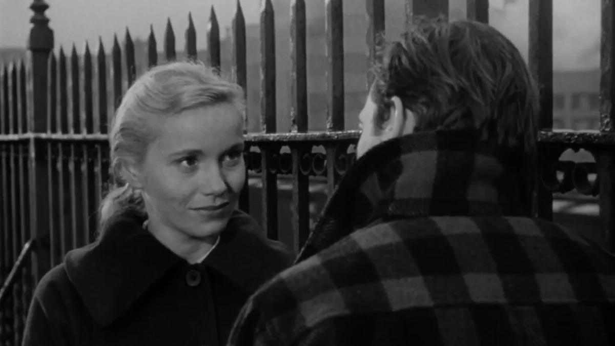 Eva Marie Saint looks at Marlon Brando beside an iron fence in a black-and-white scene