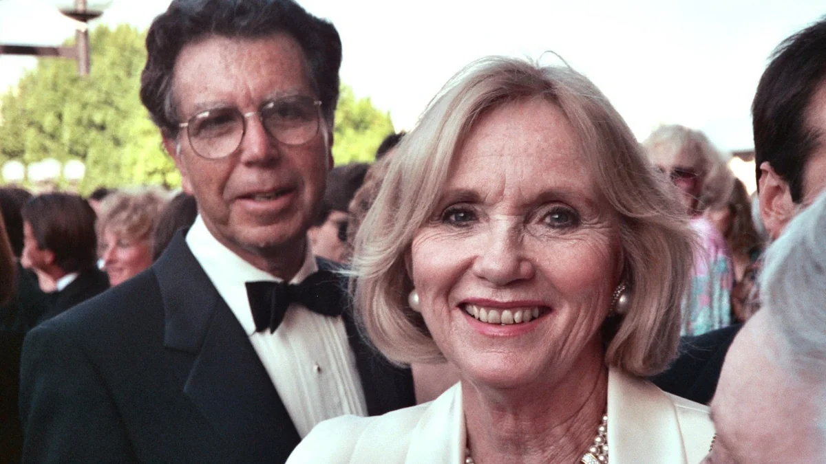 Eva Marie Saint smiles at the camera wearing pearls and light-colored clothing, with Jeffrey Hayden behind her in formal dress