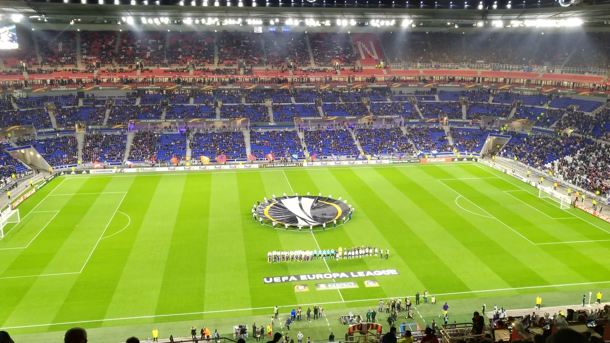 Joueurs alignés sur la pelouse avant un match de Ligue Europa dans un stade éclairé